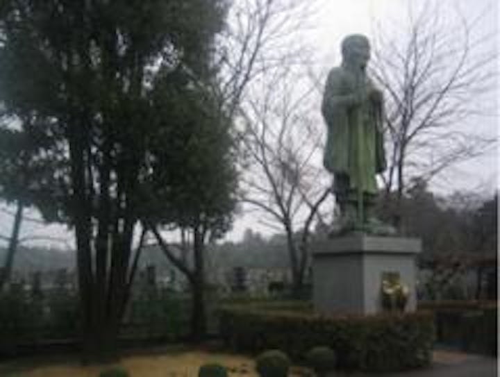 グリーンの芝地と墓地の境に立つ法然上人像。墓地全体は部厚な杉木立で囲まれていて、喧噪からはいっさい遮断されている